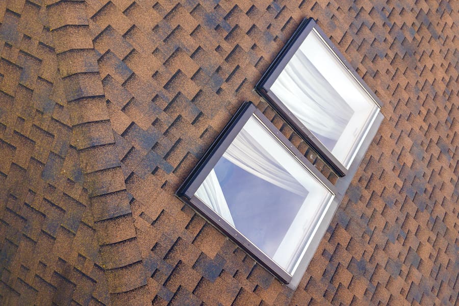 Close-up of new small attic plastic windows installed in brown shingled house roof.